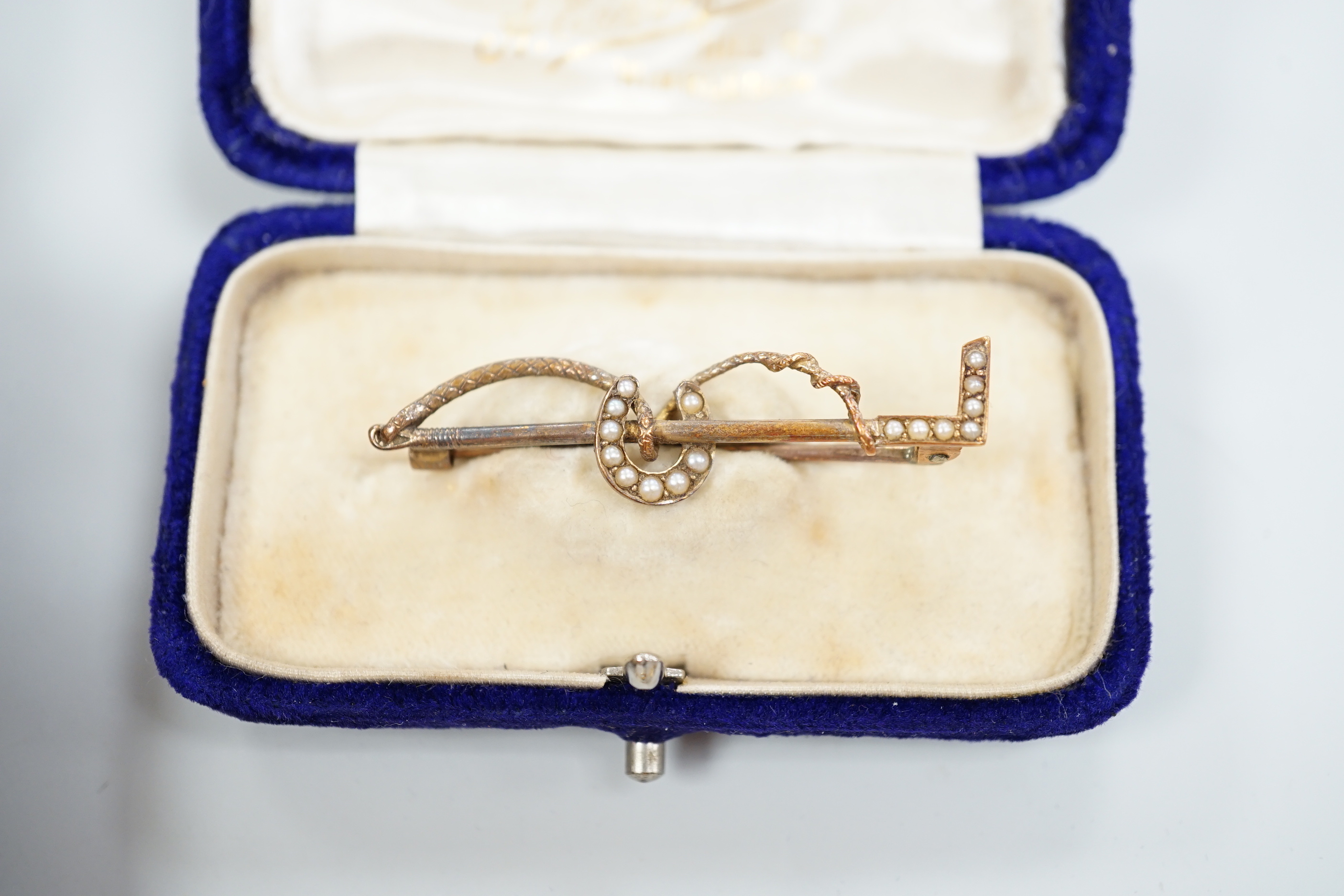 An Edwardian enamel and diamond set 'horse and jockey' stick pin, 63mm, a yellow metal and seed pearl set 'crescent and staff, brooch and a 'riding crop and horseshoe' brooch.